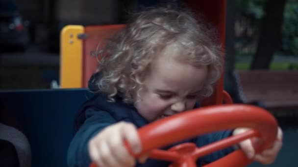 Der Junge sitzt in einem Holzauto auf dem Spielplatz und spielt. die Kamera überwacht das Kind, das in einem Spielzeugauto sitzt. — Stockvideo