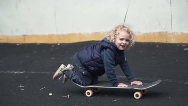 Söt liten pojke Rider sitter på skateboard i slowmotion. Närbild shot. — Stockvideo
