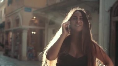 Genç şık kadın gün batımında yürüyüş ve telefonda konuşuyor. Joyful hipster kız cep telefonu açık havada kullanarak