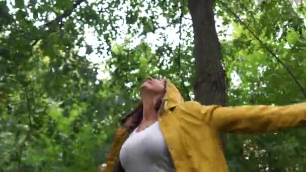 Krásná dívka ve žlutém kabátku, užívajícím teplý déšť. Žena klade tvář pod padající kapky a vrty — Stock video