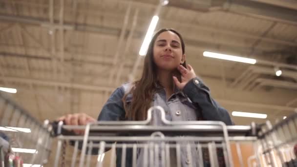 Pretty kvinna i casual kläder går i livsmedelsbutik styrning shoppingvagn med mat inne i den och tittar runt på hyllor med produkter. Kvinnor och butiker Concept. — Stockvideo