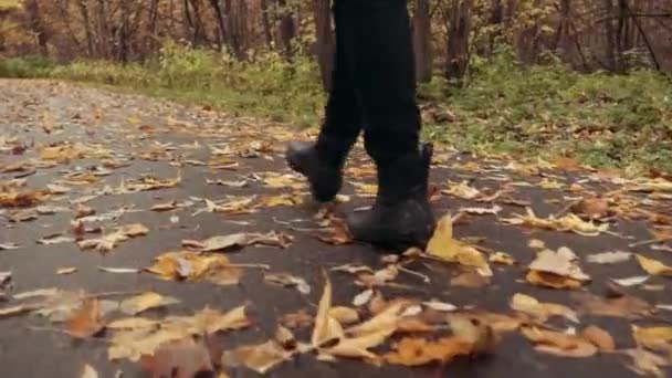 秋の公園で黄色の葉の上に男の子の足のクローズアップ。森の中の黄色の落ち葉を少女が通り過ぎる. — ストック動画