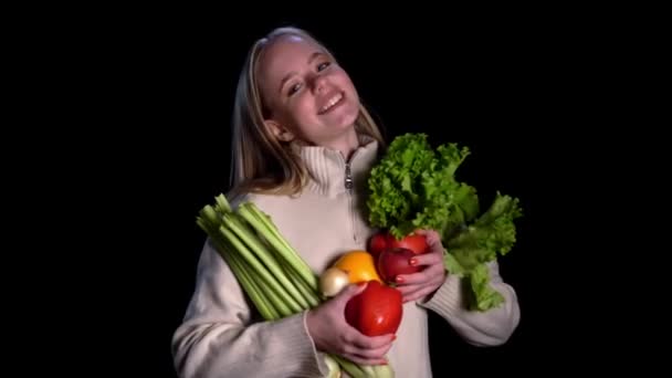 Menina bonita segurando um legumes limpos na mão, no fundo preto. Conceito: alimentos saudáveis, biologia, produtos biológicos, bioecologia, cultivar legumes, produtos naturais puros e frescos — Vídeo de Stock