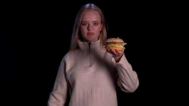 Het meisje kijkt walgelijk naar de hamburger. Slecht fastfood. Meisje op dieet. — Stockvideo