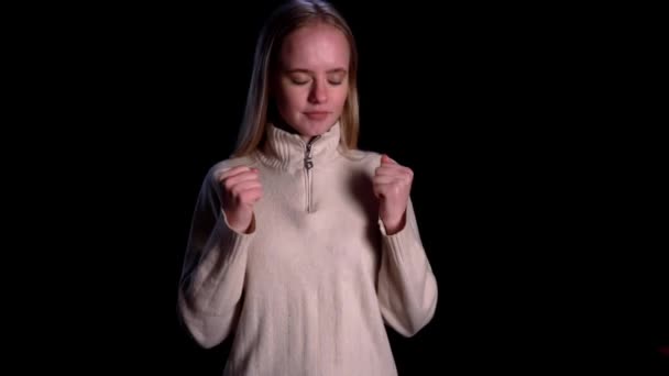 Fiatal aggódó lány áll keresztbe tett ujjakkal, hogy szerencsét hozzon, és nyer elszigetelt fekete háttér — Stock videók