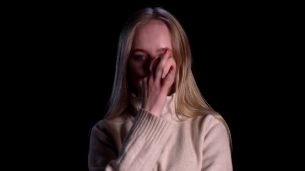 Close-up van blondine vrouw in wit trui geheim te houden en te kijken naar de camera over zwarte achtergrond — Stockvideo