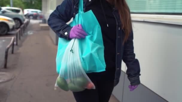 Entrega de alimentos jovem mulher em máscara protetora e luvas carrega saco com produtos da loja. Conceito de coronavírus pandêmico — Vídeo de Stock