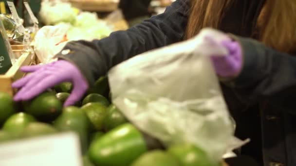 Женщина в медицинских защитных перчатках выбирает авокадо в супермаркете. индивидуальная защита от кокороновируса, натуральные витамины во время эпидемии — стоковое видео