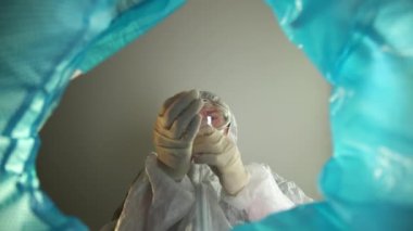 Koronavirüs üzerindeki karantina zaferinin sonu. Çöp kutusundan bir doktor tıbbi maske ve lateks eldivenleri çıkarıp atıyor. Tek kullanımlık kişisel koruyucu ekipmanlı çöp tenekesi