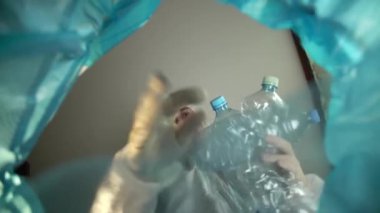 Çöp kutusundan bakınca koruyucu giysili bir adam plastik şişeleri ayrı bir plastik atık yığınına atıyor. Plastik şişeli bir çöp kutusu. Çevre koruma kavramı