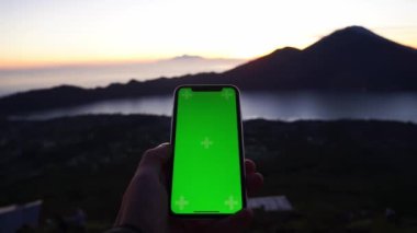 Manzarada erkek eller akıllı telefonları dikey pozisyonda tutuyor. Dağların muhteşem manzarasında yeşil ekran telefonuyla yakın çekim yapan adamlar. Gün batımı. Seyahat.