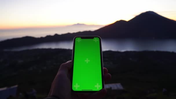 Manzarada erkek eller akıllı telefonları dikey pozisyonda tutuyor. Dağların muhteşem manzarasında yeşil ekran telefonuyla yakın çekim yapan adamlar. Gün batımı. Seyahat. — Stok video