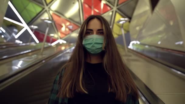 Mujer joven con una máscara protectora contra el virus escalando escaleras mecánicas en el transporte público — Vídeos de Stock