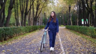 Sonbahar parkında bisiklet süren spor kostümlü bir kadın. Güneşli bir günde parkta bisiklete binen mutlu gezgin kız. Aktif, sağlıklı, açık hava sporları eğlence aktivitesi. Özgürlük, Seyahat, Seyahat. Sağlık hizmeti, özgünlük