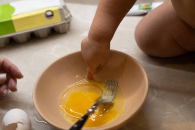 Çocuk öğle vakti mutfak ortamında çatalla yumurta sarısını zevkle keşfediyor.