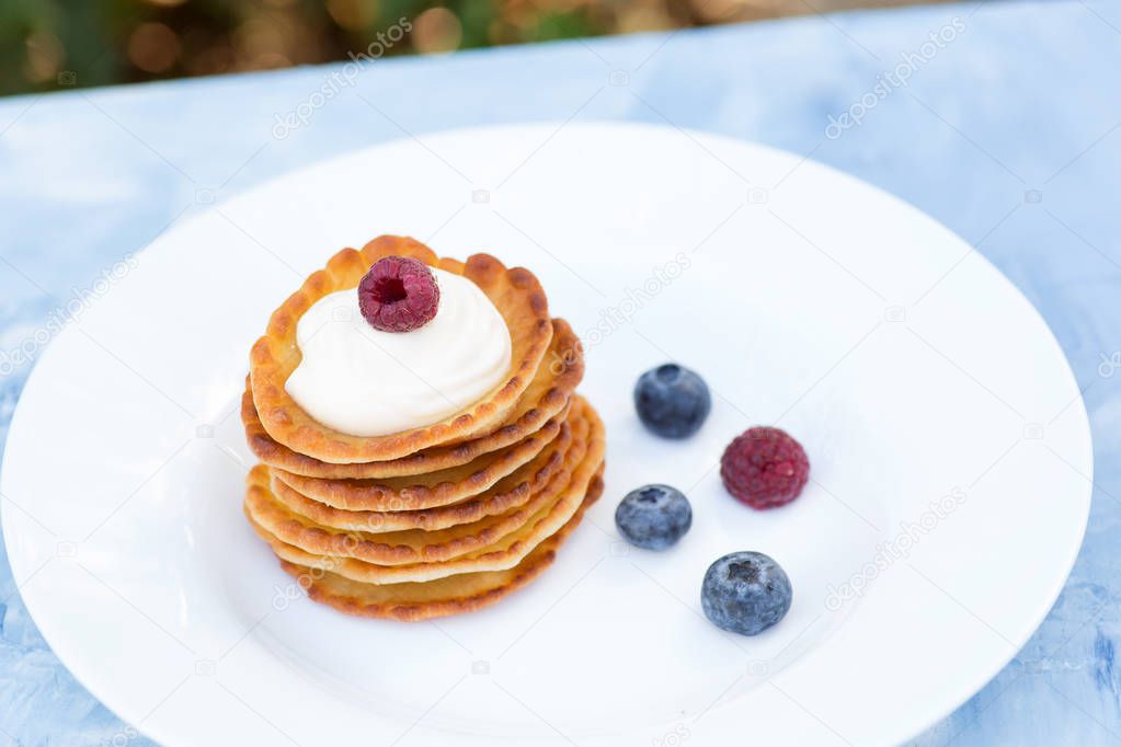 A stack of delicious pancakes with sour cream, raspberries and blueberries on a light background. with copy space