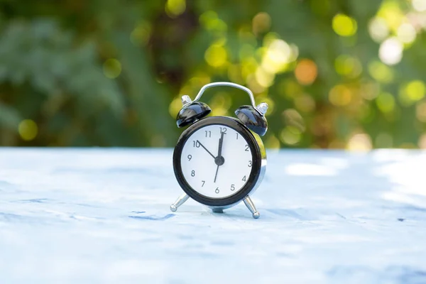 Wekker op een lichte ondergrond op een natuurlijke achtergrond. Zomer concept — Stockfoto