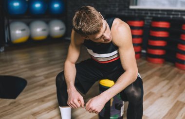Sporty man sitting on sandbag relaxing after exercises in the gym. Attractive athletic male rest after hard workout with weight training with copy space for your text or advertising. clipart