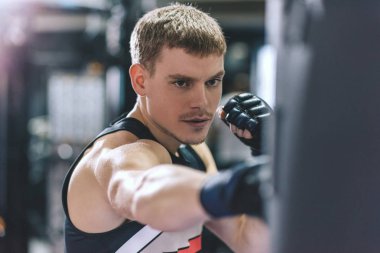 Atletik adam kickboxing eldivenli bir çanta içinde jimnastik salonu iş delme yan görünüm. Spor, yaşam tarzı, insan ve motivasyon kavramı.