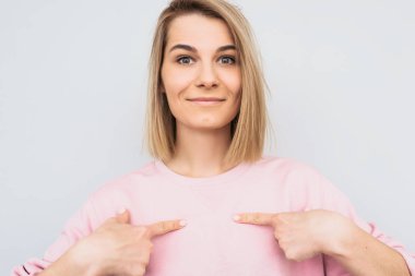 Gülümseyen güzel sarışın kadın portre çekim kendini boş kopya alanı pembe kazak, gösterir, beyaz duvardan izole bir şey tanıtır. İnsanlar ve reklam kavramı. 