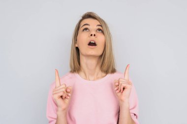 Yatay hayran genç erkek portresi yukarı forefingers, beton studio arka plan üzerinde izole rahat pembe kazak giymiş olduğunu gösterir. Kopya alanı reklam veya metin için.