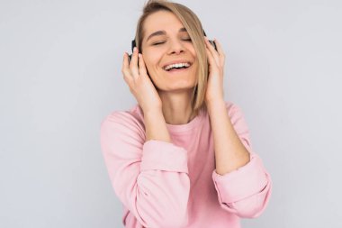 Mutlu genç erkek portre stüdyo portre kulaklık beyaz arka plan üzerinde izole favori müzik eliyle tutarak kapalı gözlerle pembe elbise giyer. Kopya alanı reklam için