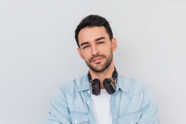 Yakışıklı genç beyaz portre rahat mavi gömleğive beyaz giyen erkek T-shirt, kulaklıklar var, en sevdiğiniz müzik dinliyor, güvenle kameraya benziyor. Kopya alanı metin veya reklam için.