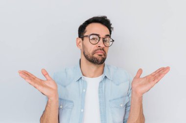 Trendy yuvarlak gözlük takıyor demin mavi gömlek, omuz silkiyor belirsiz genç şık anız adam portresi şaşkın omuz veya karıştı. Beyaz emin erkek jestleri şüpheyle el ile yapmak.