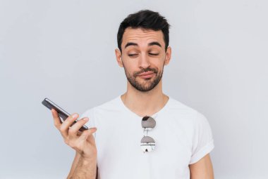 Stüdyo portre rahatsız Genç beyaz tonları ve onun cep telefonu pil çalışan aşağı ya da yüksek sesle konuşma nedeniyle tiksinti beyaz kolsuz tshirt adam sakallı. İnsanlar, teknoloji