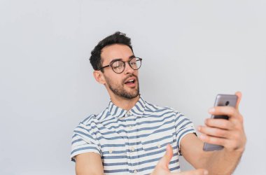 Mutlu genç Avrupa sakallı adam selfie yapma ve neşeli gülümseme ile ekrana bakarak newsfeed kullanarak akıllı telefon, sosyal ağlar üzerinden tarama çizgili gömlek ve yuvarlak gözlük takıyor. İnsanlar kavramı