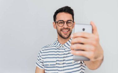 Beyaz arka plan mavi çizgili gömlek giymiş Kafkas erkek poz selfie mutlu gülümsemeyle için şık yuvarlak gözlük yatay portresi. Kişi, yaşam tarzı ve modern teknoloji kavramı.