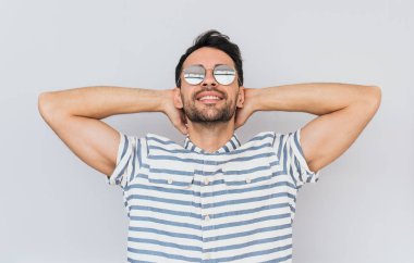 Trendy yuvarlak ayna güneş gözlüğü takıyor ve rahat gömlek iyi yaz havanın tadını beyaz stüdyo arka planı poz şeritli tıraşsız yakışıklı erkek modeli. Kişi, yaşam tarzı ve duygular kavramı