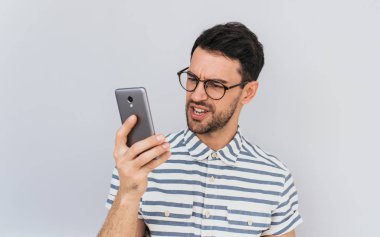 Kızgın sakallı yakışıklı işadamı portresi yuvarlak gözlük ve rahat gömlek giyer, cep telefonu, beyaz stüdyo duvar arka plan üzerinde poz içine öfkeli görünüyor. İnsanlar, duygu, teknoloji kavramı