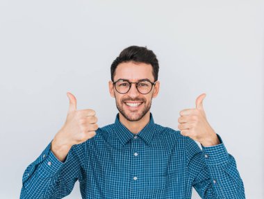 Sağlıklı dişlek sağlıklı gülümseme, yakışıklı erkek ile her iki el başparmak gösterilmesini kameraya mutlu ifade ile seyir yuvarlak trendy gözlük, mavi gömlek giyer. Beden dili, duygu kavramı