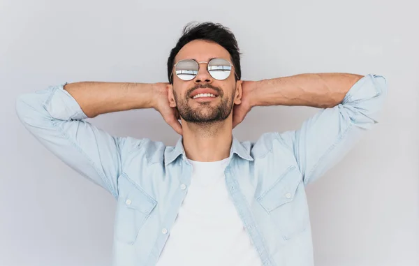 Tıraşsız yakışıklı erkek model giyen trendy yuvarlak ayna güneş gözlüğü ve mavi rahat gömlek beyaz stüdyo arka planı poz yatay portresi. Kişi, yaşam tarzı ve duygular kavramı