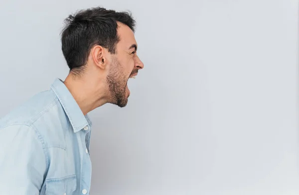 Yan görünüm portre duygusal deli şık genç erkek bağırır yüksek sesle ve öfkeyle, stresli, beyaz arka plan üzerinde izole olumsuz duygular ifade eder. Duygular, duygular ve insanlar kavramı