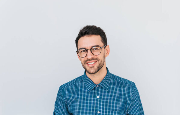 Portrait of handsome smart-looking smiling male posing for social advertisement wearing blue shirt and glasses, isolated on white background with copy space for your promotional information or content