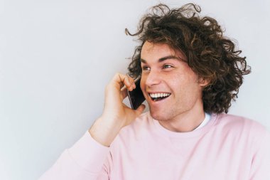 Kıvırcık saçlı mutlu neşeli erkek portre çekim ile arkadaş cep telefonu üzerinden iletişim vardır. Gülümseyen ve spreaking akıllı telefon üzerinden gülerek yakışıklı adam. İnsanlar, teknoloji kavramı.
