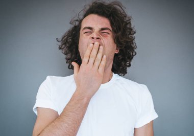 Yorgun ya da bıkkın beyaz genç erkek modeli kıvırcık saçlı esneme sırasında ağız kapsayan portresi, duygu aşırı iş yükü sonra bitkin. Derslerinizden sonra uykulu göz olan öğrenci şık adam.