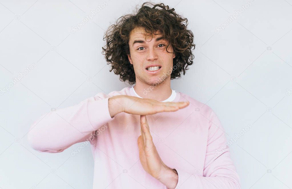 Horizontal portrait of serious male shows stop gesture, asks not to bother him, isolated over white background. Handsome grumpy male shows time out with copy space for your advertisment.