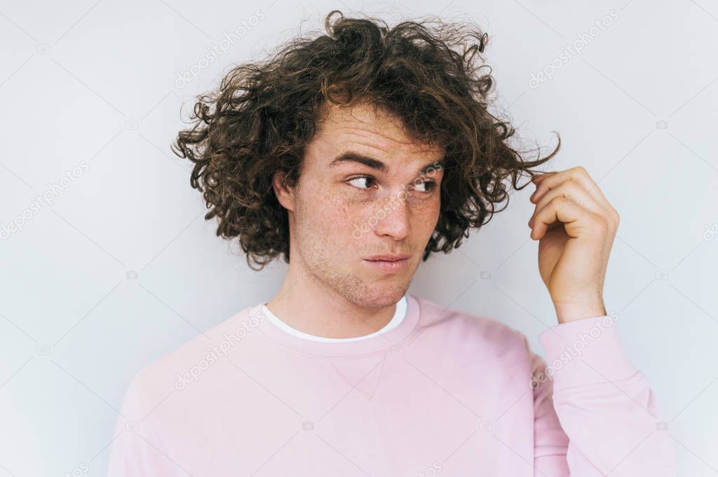 Horizontal closeup portrait of stylish unhappy male with curly hair poses in studio against white background, shows his damage hair, need treatment. Disagreement and negative expressions.