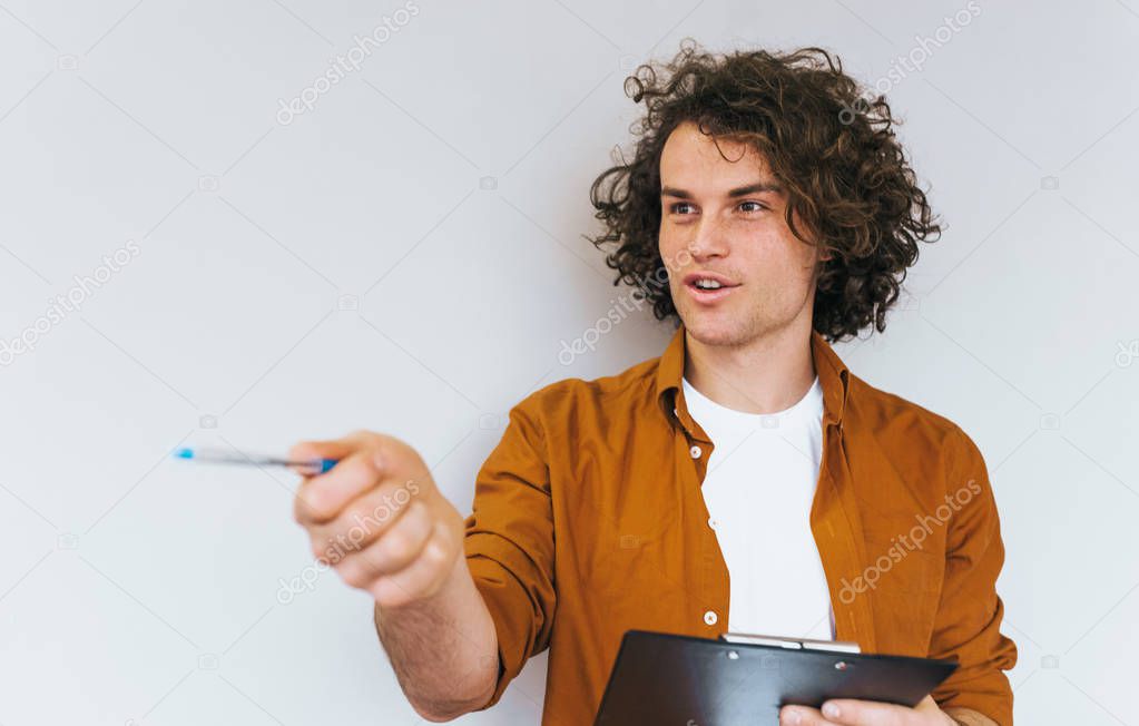 Closeup portrait of handsome businessman with curly hair, thinking on plan for next week, wearing white t-shirt and shirt. Busy manager male makes notes in notebook for booking and shipping orders 