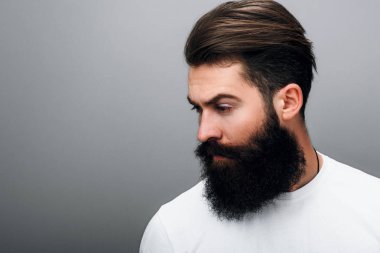 Yan görünüm yakışıklı acımasız eril genç erkek arayan bir yana, bir gri studio arka plan üzerinde poz sakallı. Portre genç Avrupa moda trendy sakal berber.