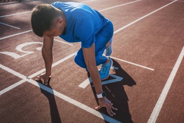 Side view of young male athlete at starting block on running track. Caucasian sprinter man in starting position for running to start a race at stadium. Sport, lifestyle and people concept. clipart
