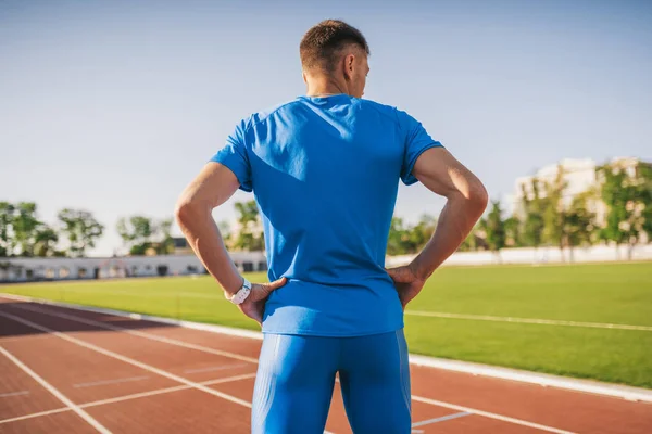 水平背面よそ見ヒップの彼の手によって立っているプロの男性スポーツ選手 白人スプリンターは 屋外の競技場で 陸上競技用トラックで並んで立っています スポーツ ライフ スタイル — ストック写真