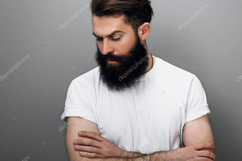 Cropped horizontal portrait of handsome Caucyoung bearded man looking down, on a gray studio background. Portrait of young European hipster with trendy beard. 