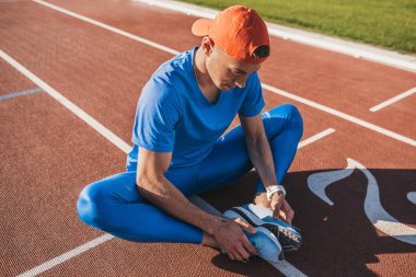 Yatay atış beyaz atlet koşu parkuru üzerinde oturan germe egzersizleri yapıyor. Birlikte kaçmak için hazırlanıyor ya da egzersiz yaptıktan sonra rahatlatıcı katıldı ayaklı koşu parkuru üzerinde oturan runner adam