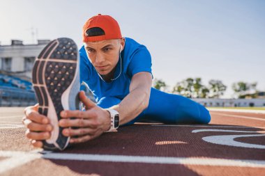 Çalışma dışarı için hazırlanması üzerinde yarış pisti Stadyumu, onun bacak Germe atlet runner genç erkek görüntüsünü kapatın. Beyaz adam açık havada mavi spor giyim giymiş egzersiz. Spor, insan, yaşam