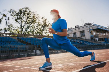 Çalışma dışarı hazırlama bir koşu parkuru Stadyumu, tarih onun bacak Germe sporcu genç erkek. Beyaz adam açık havada mavi spor giyim giymiş egzersiz. Spor ve insanlar