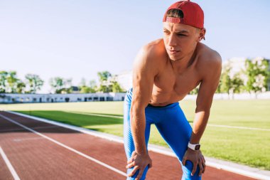 İnsanlar ve spor kavram. Yakışıklı sporcu erkek rahatlatıcı bir atış üstsüz stadyum üzerinde yoğun egzersiz yaptıktan sonra kapatın. Elleriyle dizlerinin üstüne bir koşu sonra dinlenme dinlenme alarak ve açık koşmak runner.
